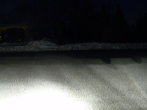 1988 Ford Bronco - A dark, snowy landscape is illuminated by bright headlights, with a website logo visible in the lower right corner.