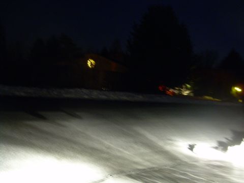 1988 Ford Bronco - Headlights illuminate a snowy road at night, with a house and a distant vehicle visible.