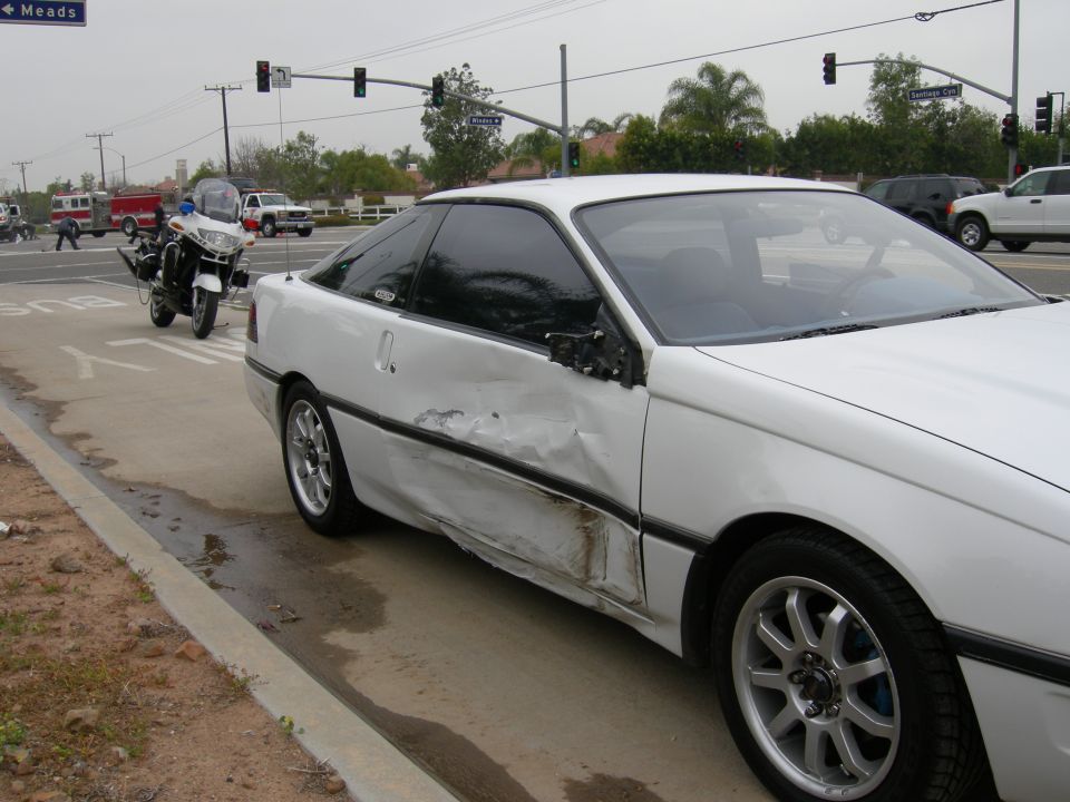 White coupe with side damage at an intersection with emergency vehicles