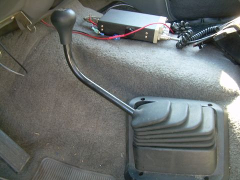 1988 Ford Bronco - Floor-level interior shot of a manual transmission shifter with a bent black lever and round knob rising from a ribbed rubber boot on gray…