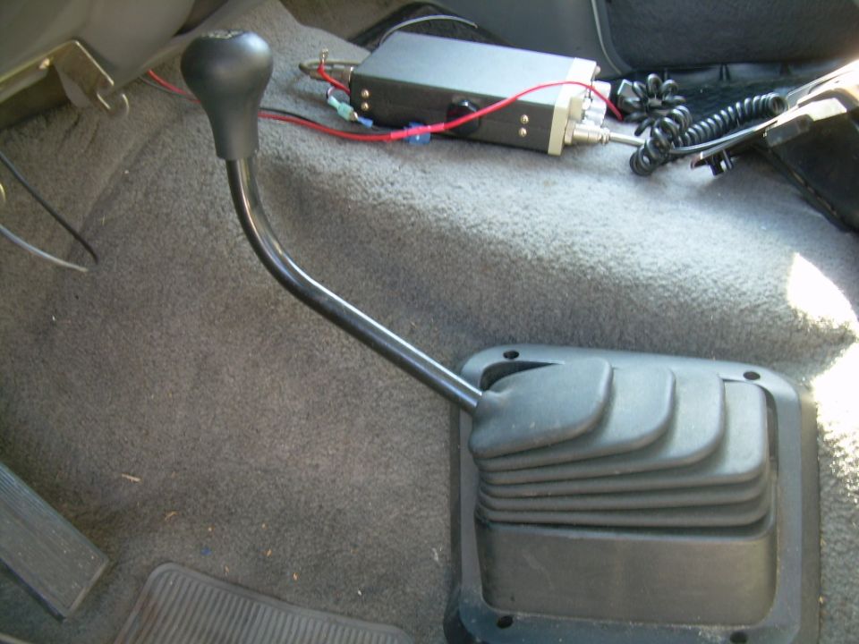 Manual shifter with rubber boot on gray carpet next to a mounted CB radio