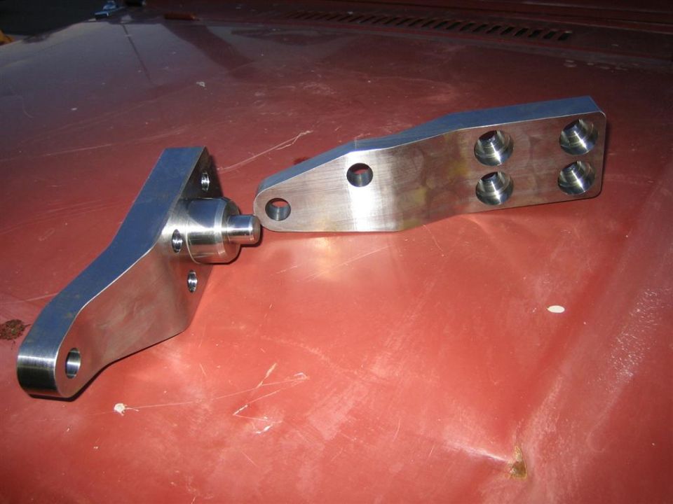 Two custom metal suspension parts on a red surface