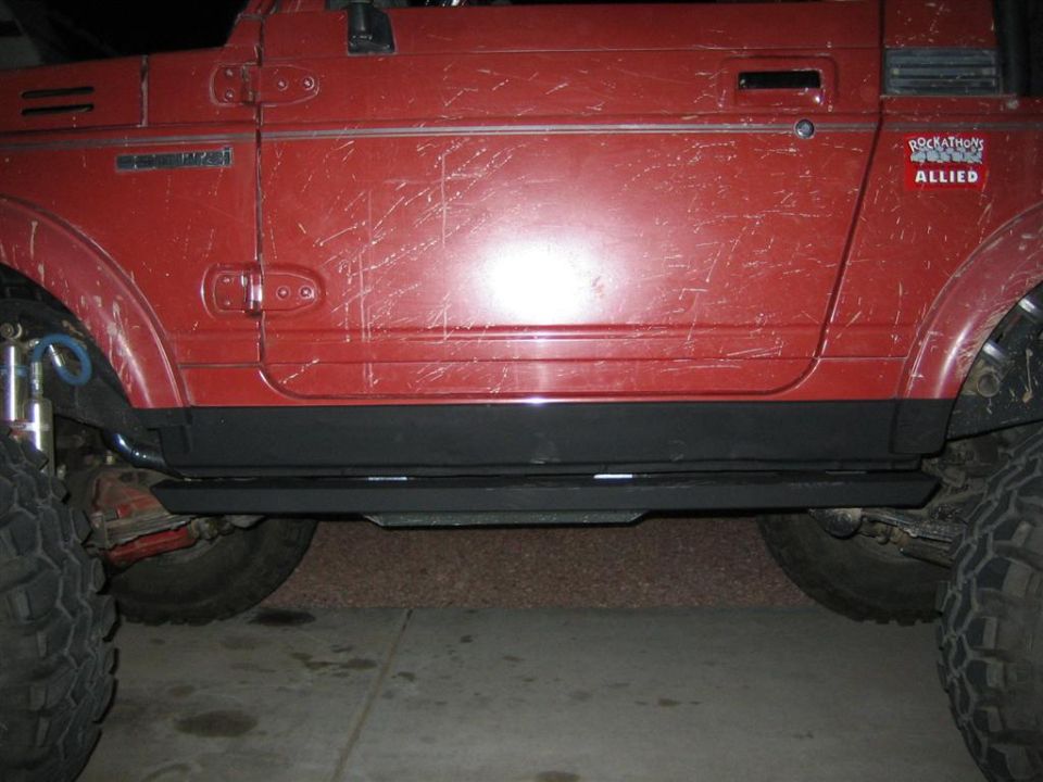 Red off-road vehicle side view showing sliders, large tires, and body scratches. A "ROCKATHON ALLIED" sticker is visible
