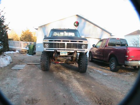 1977 Ford F-250 - A lifted 1977 Ford F-250 pickup truck is parked in front of a garage, with another pickup truck to its right.