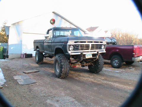 1977 Ford F-250 - This lifted 1977 Ford F-250 pickup truck is parked outside a garage, with another truck visible in the background.