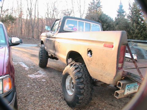 1977 Ford F-250 - A lifted pickup truck is parked on a gravel surface, with another vehicle partially visible to its left.