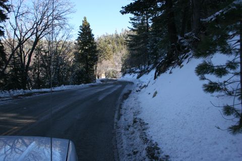 1996 Ford Bronco - A car drives on a snow-dusted road through a wooded area.