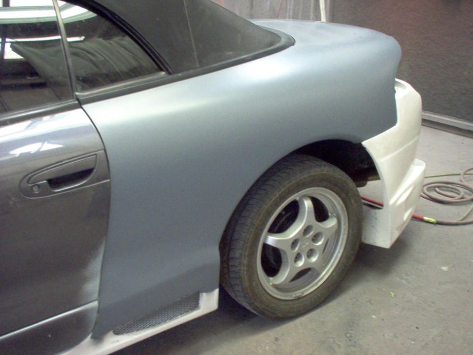 car's rear quarter panel and door in primer, with a black soft top visible