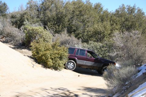 1996 Ford Bronco - A maroon SUV navigates a dusty, off-road trail surrounded by dry brush and scattered patches of snow.