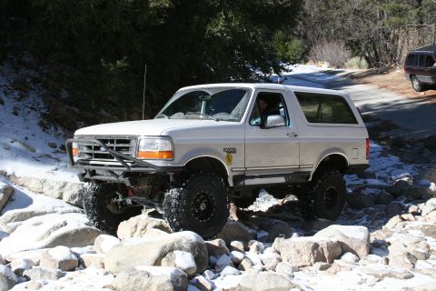 1996 Ford Bronco - A silver 1996 Ford Bronco navigates a rocky trail with snow patches.