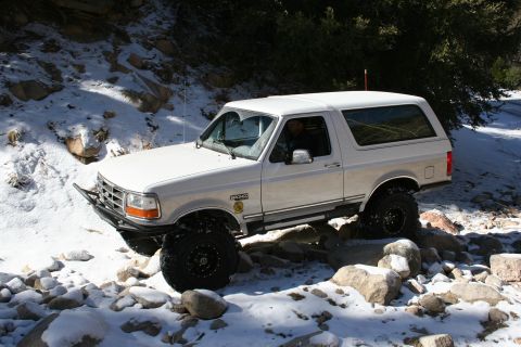 1996 Ford Bronco - A white 1996 Ford Bronco tackles a rocky, snow-covered trail, its off-road capabilities.