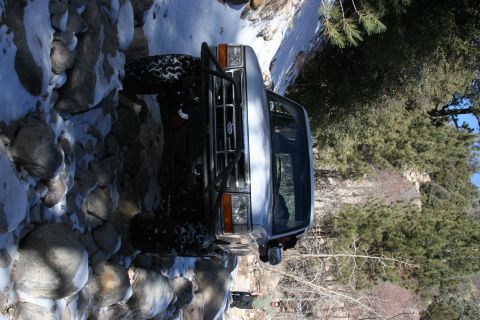 1996 Ford Bronco - A silver SUV navigates a challenging rocky and snowy path in a wooded area.