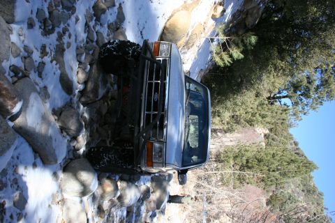 1996 Ford Bronco - A silver 1996 Ford Bronco navigates a challenging off-road path through a creek filled with rocks and snow.