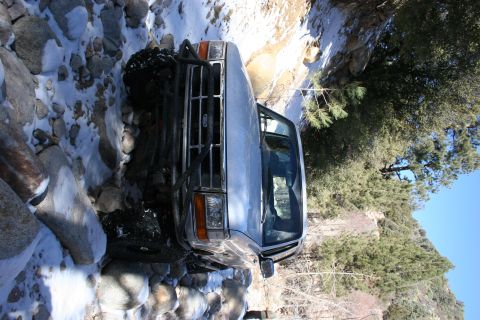 1996 Ford Bronco - 1996 Ford Bronco navigating a challenging off-road trail in a creek bed with snow and rocks.