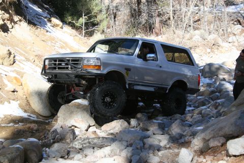 1996 Ford Bronco - A silver 1996 Ford Bronco tackles a challenging, rocky off-road path with snow patches visible.