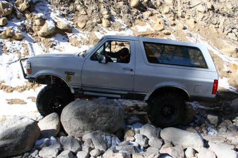 1996 Ford Bronco - A silver 1996 Ford Bronco tackles a challenging off-road course with large rocks and patches of snow.