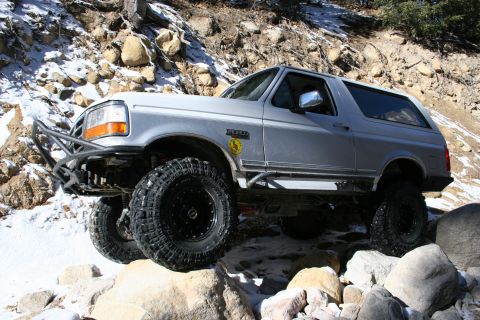1996 Ford Bronco - A silver 1996 Ford Bronco tackles a challenging off-road path covered in snow and rocks.