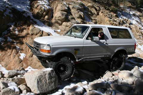 1996 Ford Bronco - A white 1996 Ford Bronco is shown traversing a difficult, rocky terrain with patches of snow.
