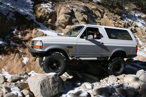 1996 Ford Bronco - A white 1996 Ford Bronco navigates a challenging rocky terrain with snow patches.