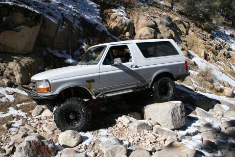 1996 Ford Bronco - A white Ford Bronco navigates a challenging rocky terrain with snow patches.