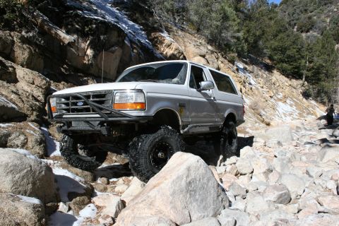 1996 Ford Bronco - Silver 1996 Ford Bronco tackling a challenging off-road course with large rocks and sparse snow.