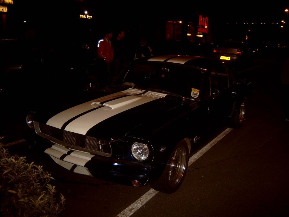 Black classic Mustang with white racing stripes at night