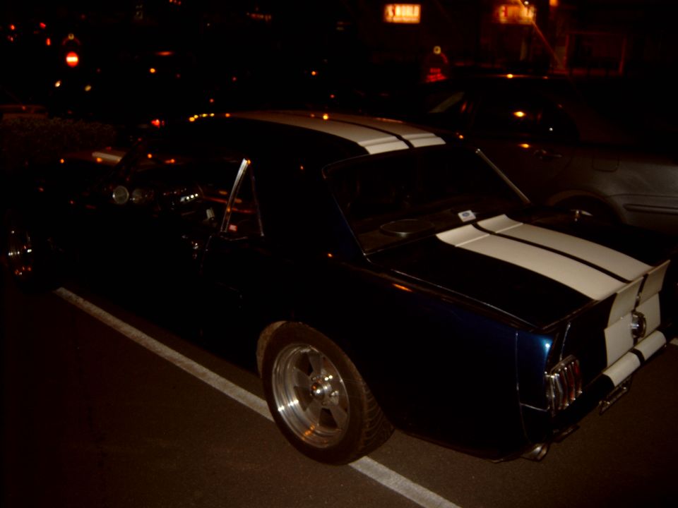 Rear three-quarter view of a black striped classic Mustang at night