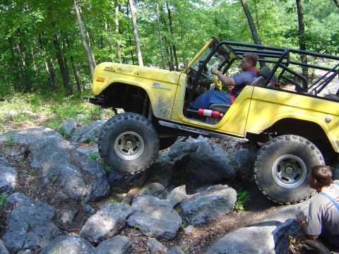 1975 Ford Bronco - A yellow 1975 Ford Bronco navigates a rocky obstacle course in a forest setting.
