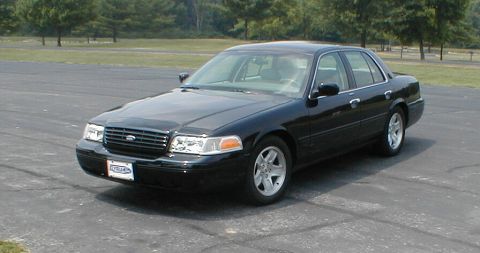 2001 Ford Crown Victoria - A black 2001 Ford Crown Victoria is shown from a three-quarter front view, parked on an asphalt surface with trees in the background.