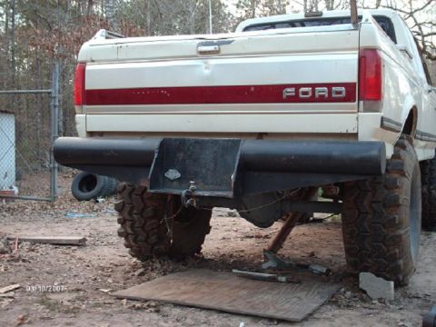 1990 Ford F-150 - The rear of a lifted Ford pickup truck is shown, a custom bumper and large off-road tires.