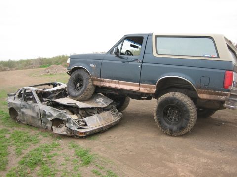 1995 Ford Bronco - Passenger-side view of a lifted two-tone blue and tan Ford Bronco with a removable hardtop, black steel wheels and mud-caked aggressive off…