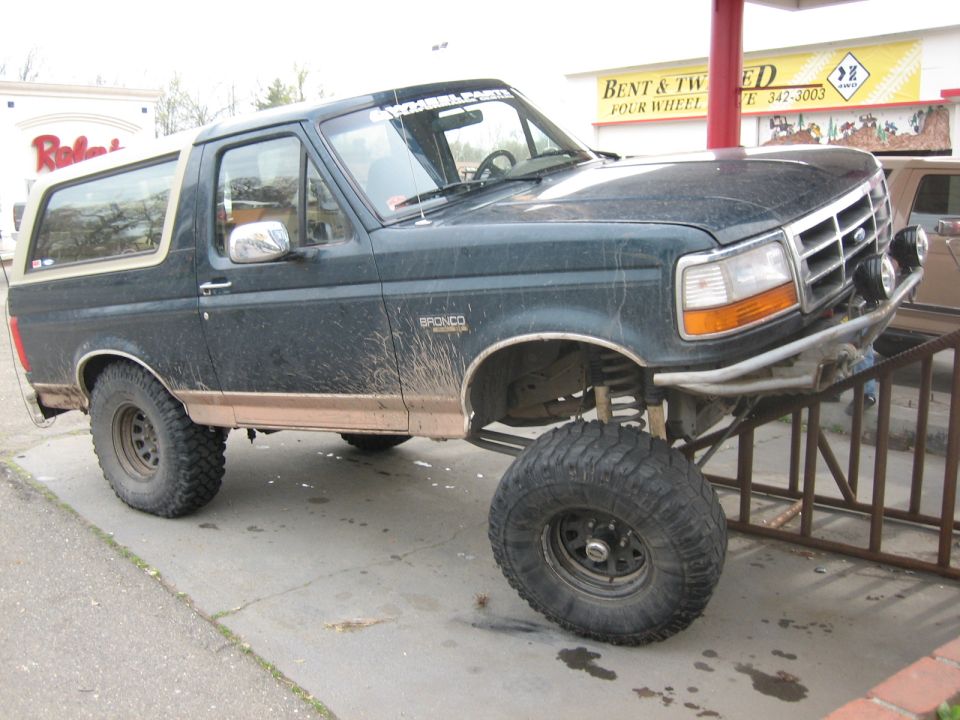 Dark green Ford Bronco with lifted suspension and large tires, parked on a ramp outside a shop