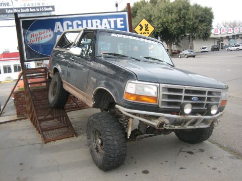 1995 Ford Bronco - Modified Ford Bronco with oversized tires and suspension sits on a ramp in front of a business.