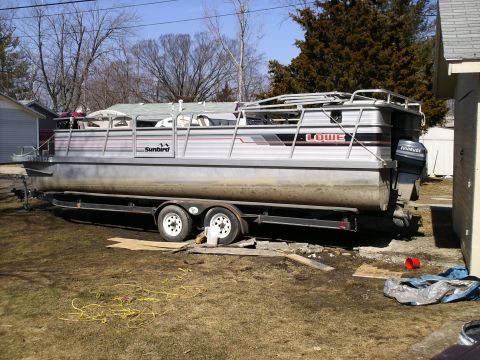 1983 Ford Bronco - A pontoon boat is parked on a trailer in a yard, with a house and trees in the background.