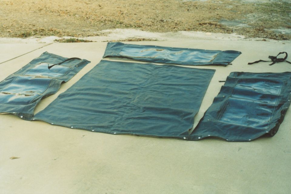 Dark blue soft top components with clear plastic windows laid out on concrete