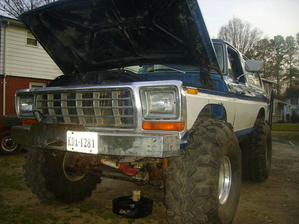 Lifted Ford truck with hood open, showing front end and large tires. License plate KDA-1281 visible