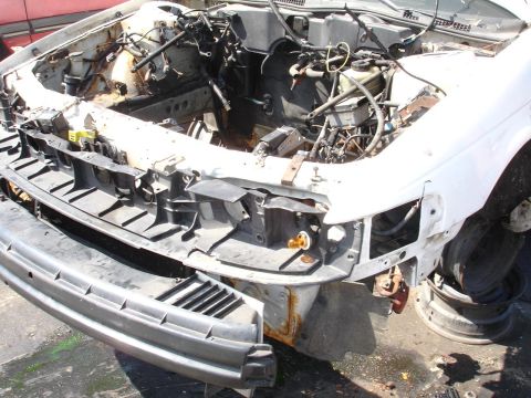 1993 Ford Taurus - The front of a white car is shown with its hood open and engine compartment exposed, indicating it is heavily damaged or dismantled.