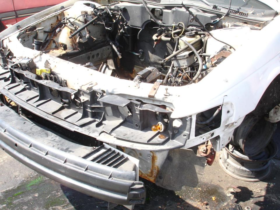 Car's front end is dismantled, showing engine bay and missing parts. Bumper is detached