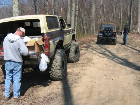1992 Ford Mustang - Two off-road vehicles, a Ford Bronco and a Jeep Wrangler, are parked on a dirt path in a wooded area.