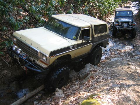 1992 Ford Mustang - A two-tone Ford Bronco navigates a rocky stream bed, followed by a Jeep on a trail.