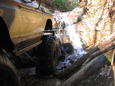 1992 Ford Mustang - Off-road vehicle navigates a rocky stream bed with a waterfall in the background.