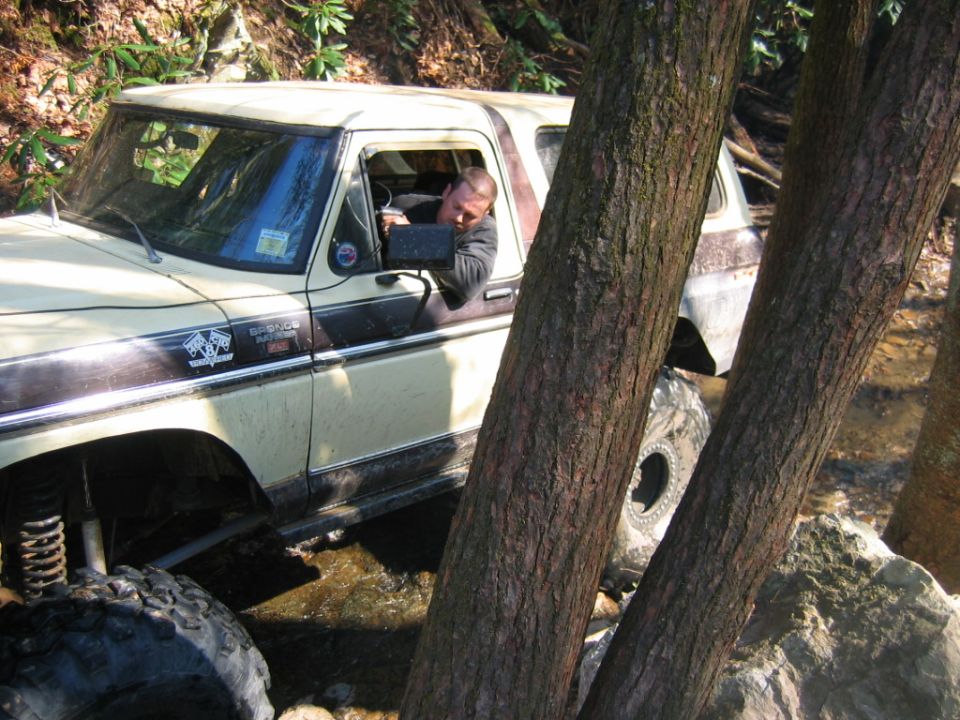 1978 Ford Bronco with lifted suspension driving through water, driver visible