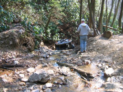 1992 Ford Mustang - An off-road vehicle is stuck in a creek bed, surrounded by trees and rocks.