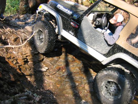 1992 Ford Mustang - Jeep Wrangler TJ tackling a challenging off-road obstacle on a muddy, rocky path.