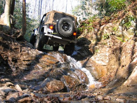 1992 Ford Mustang - Off-road Jeep Wrangler navigates a challenging rocky terrain with flowing water.