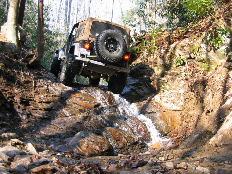 Jeep Wrangler driving through a rocky stream with water cascading over stones