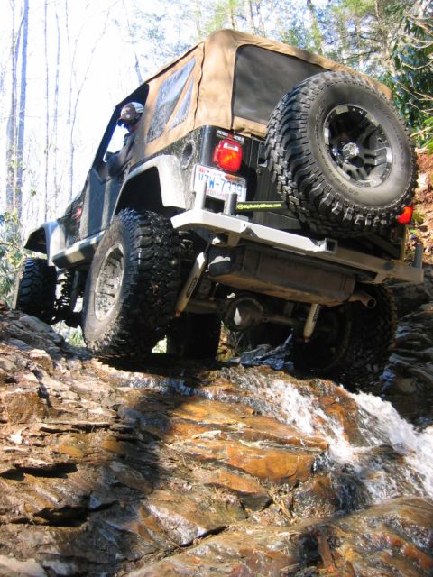1992 Ford Mustang - A Jeep Wrangler navigates a rocky stream bed on an off-road trail.