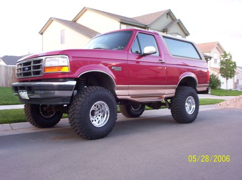 1995 Ford Bronco - This lifted 1995 Ford Bronco features large off-road tires and chrome wheels, parked on a residential street.