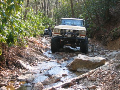 1992 Ford Mustang - An off-road vehicle navigates a challenging path through a wooded area with a stream.