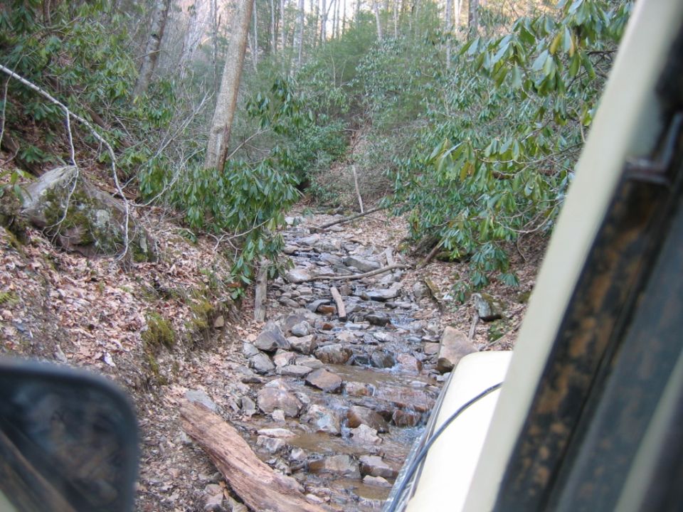 Off-road vehicle interior view looking out at a rocky stream bed in a wooded area